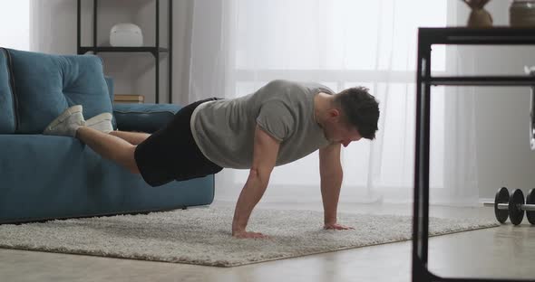 Intensive Workout at Home Man Is Doing Pushups in Living Room Leaning on Couch By Legs Keeping Fit alt