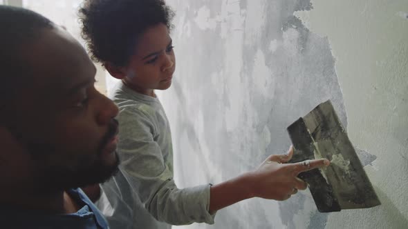 Black Man Teaching Son How to Scrape Walls alt