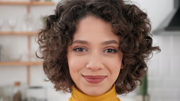 Close Up Face Smiling Hispanic Curly Woman Looking Camera at Home Kitchen alt