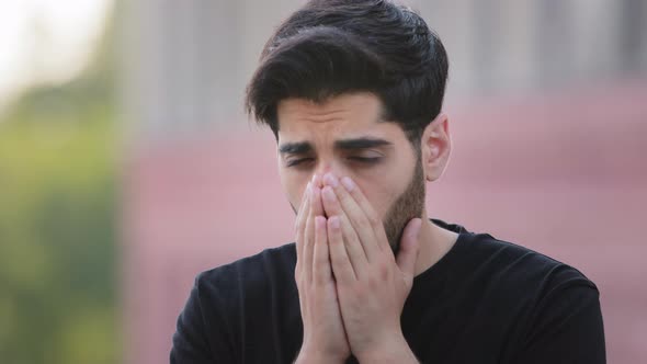 Stressed Bearded Indian Allergic Young Man Sneezing with Hands in Front of Face Outdoors alt