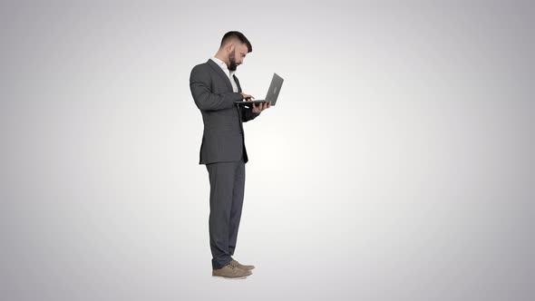 Handsome Businessman Standing and Working on Laptop on Gradient Background alt