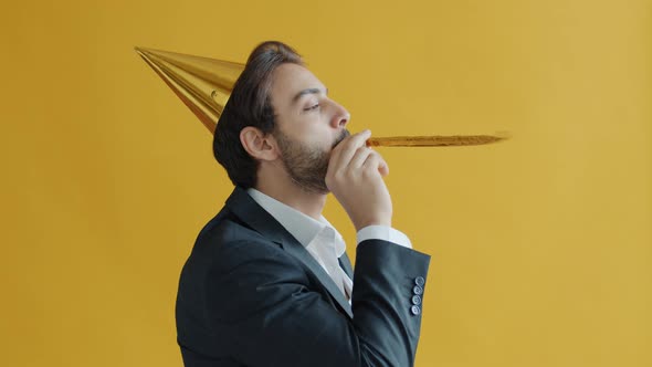 Portrait of Happy Arab Man Wearing Birthday Hat Blowing Horn Having Fun Alone on Yellow Color alt