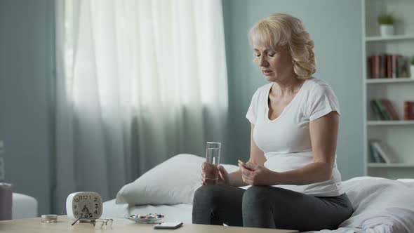 Blond Mature Female Sitting on Bed and Taking Pills, Health and Medicine alt
