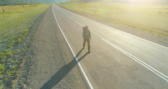 Flight Over Hitchhiker Tourist Walking on Asphalt Road. Huge Rural Valley at Summer Day. Backpack alt