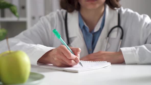Woman Doctor Writing At Her Desk. Woman, Surgeon, Nurse, Pharmacy With Stethoscope In Hospital alt