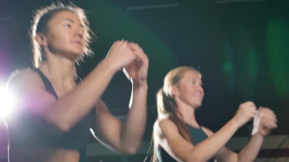 Two Athletic Women Perform a Synchronized Warmup in a Dark Gym alt