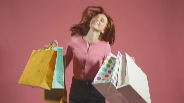 Smiling Beautiful Redhaired Woman Jumps with Happiness and Enjoys Shopping Holding Several Colorful