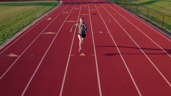 Teen girl runs on a high school track drone camera precedes alt