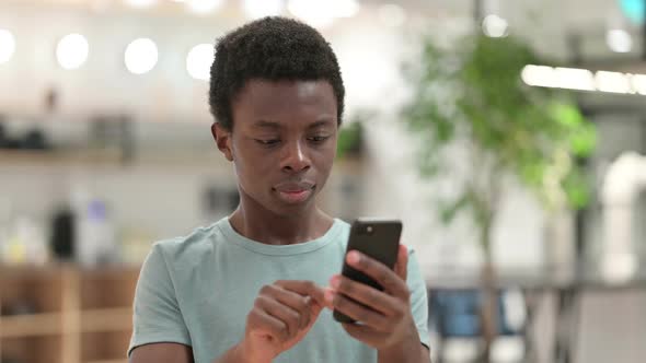 Young African Man Celebrating Success on Smartphone alt