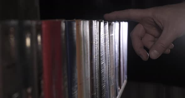 A Mans Hand is Looking for the Right Book Among a Collection of Volumes alt