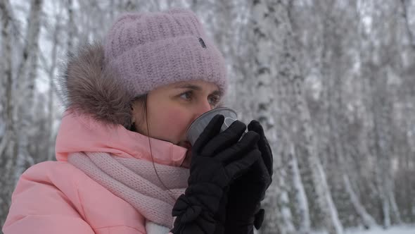 Young Woman Drinking Hot Tea in Winter Forest alt