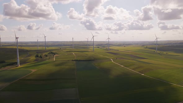 Soft clouds floating by over a wind park in rural Germany. Aerial wide angle pull back shot alt