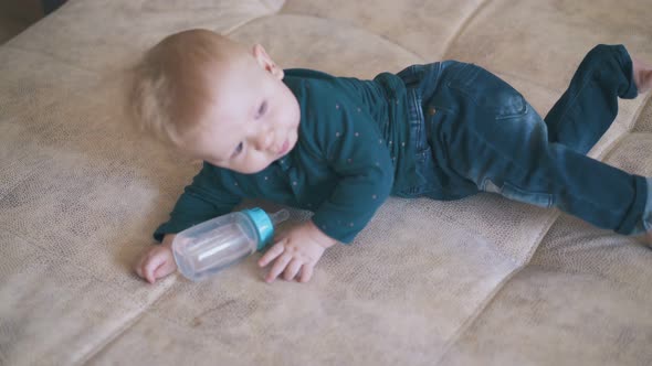Cute Child Plays with Bottle Crawling on Bed at Home alt