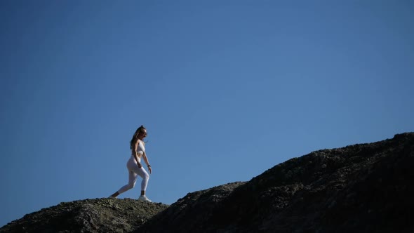 The Girl Does a Workout on the Edge of the Cliff, Jumping and Lunges. alt